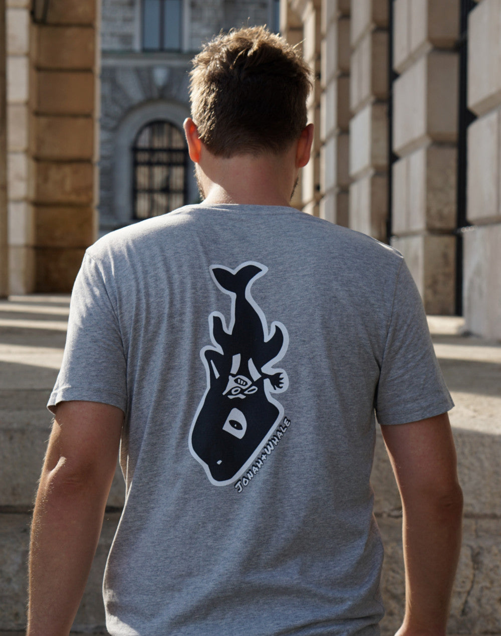 man wearing a shirt with a whale logo on back walks up the hallway stairs