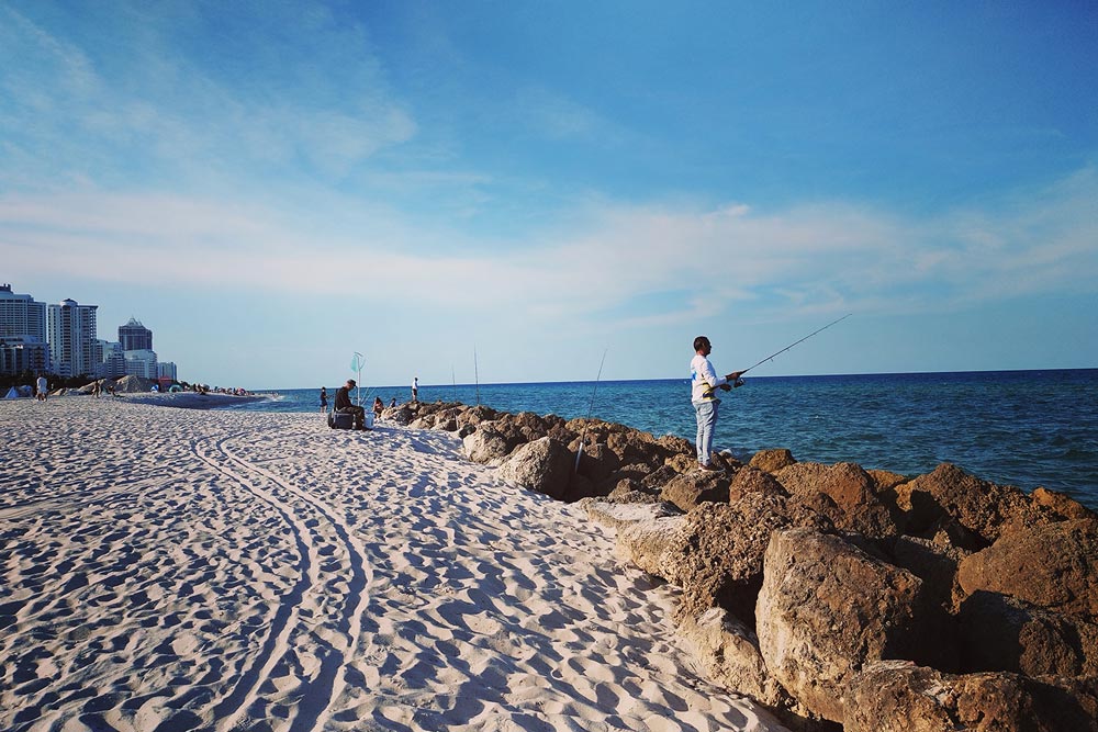 A Miami Beach resident fishes in the rocks on the beach at Mid-Beach