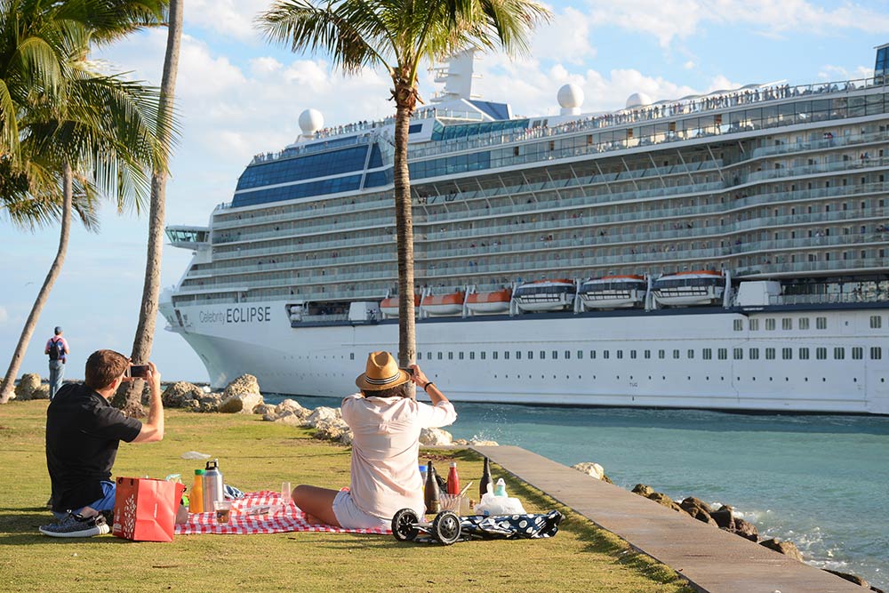 A couple picnics in South Pointe Park and watches a passing cruise ship