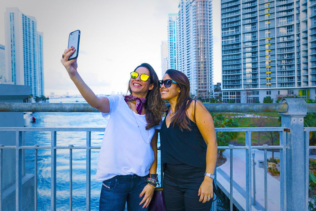 A couple of young women take a selfie on a bridge over the Miami River