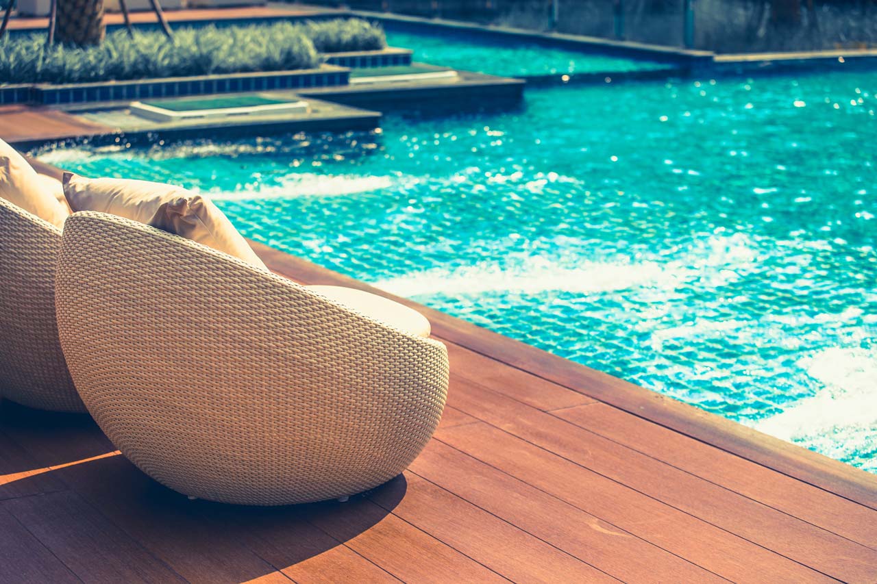 Relaxing rattan chairs with pillows beside swimming pool