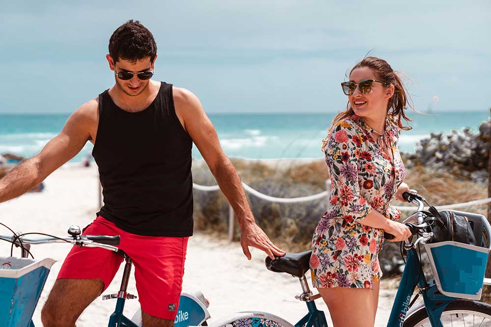 A young couple having a great time biking along the Miami Beach Boardwalk
