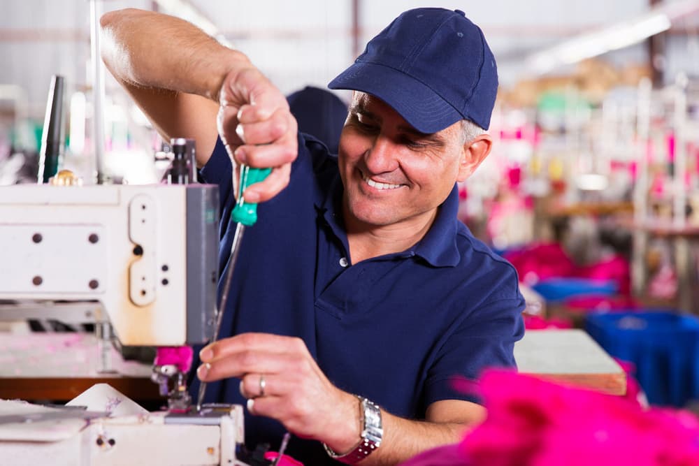 Sewing machine repairman smiling while fixing a machine