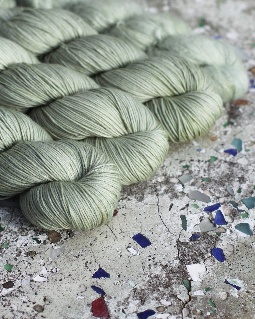 Four skeins of sage green yarn on a marbled table.