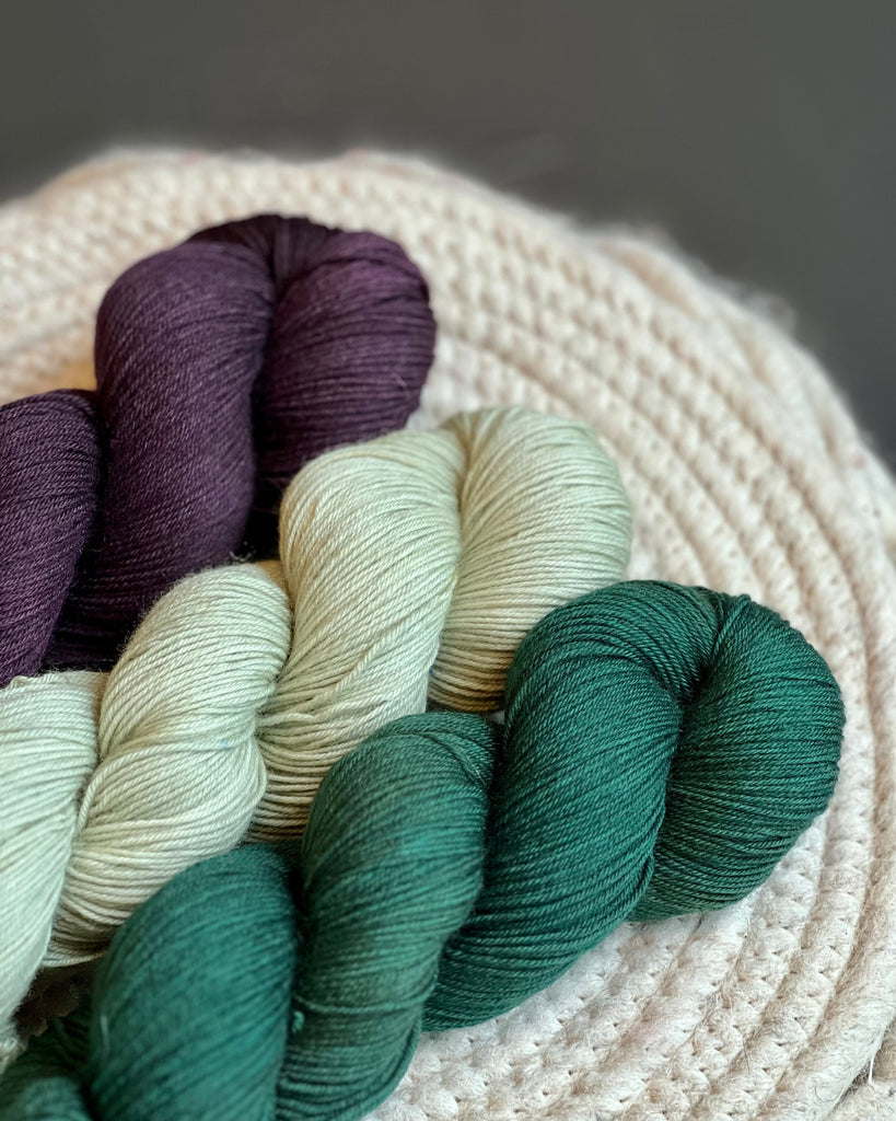 Three skeins of yarn in deep purple, sage green, and forest green.