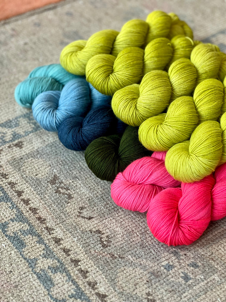 Skeins of bright green yarn shown atop blue, dark green, and pink skeins of yarn.