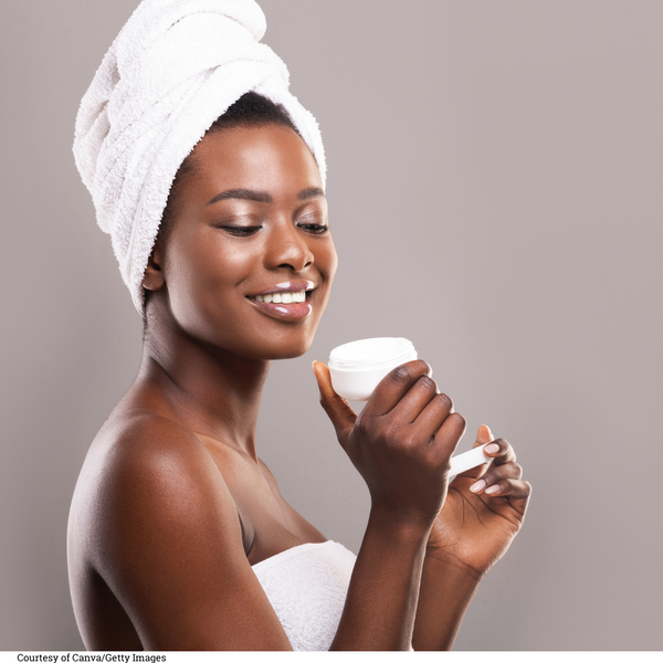 Black woman with towel wrapped around hair smiling while looking at a jar of moisturizer