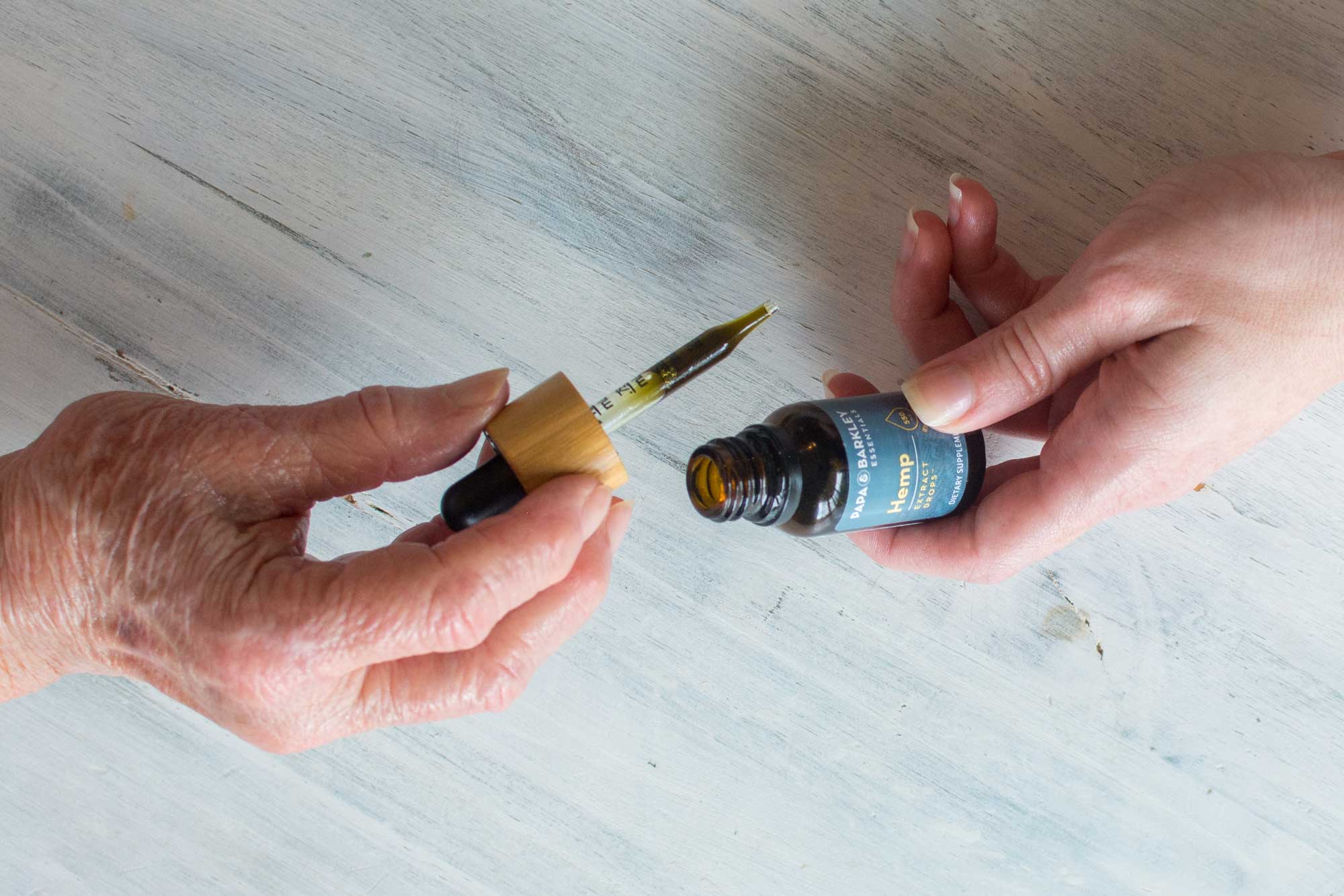 Generational elderly woman holding CBD tincture dropper while granddaughter holds bottle