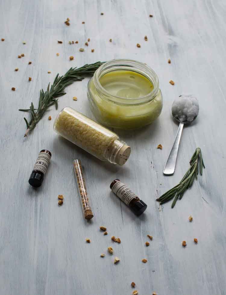 Styled ingredients of hemp oil body butter with beeswax, essential oils, coconut oil, and dried herbs