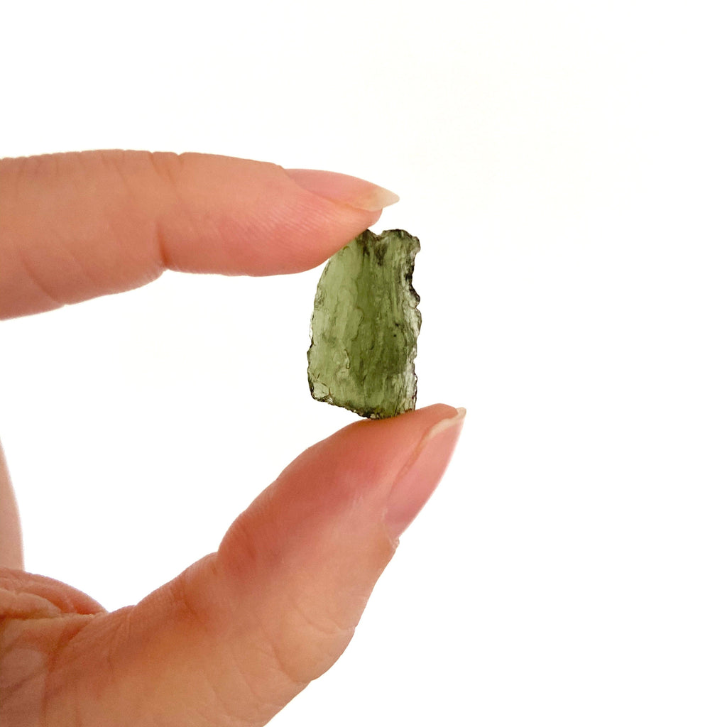 woman's fingers holding a peice of natural moldavite gemstone crystal meteorite