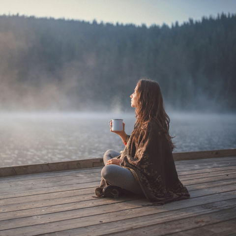 Woman practicing gratitude by the water with her coffee at sunrise