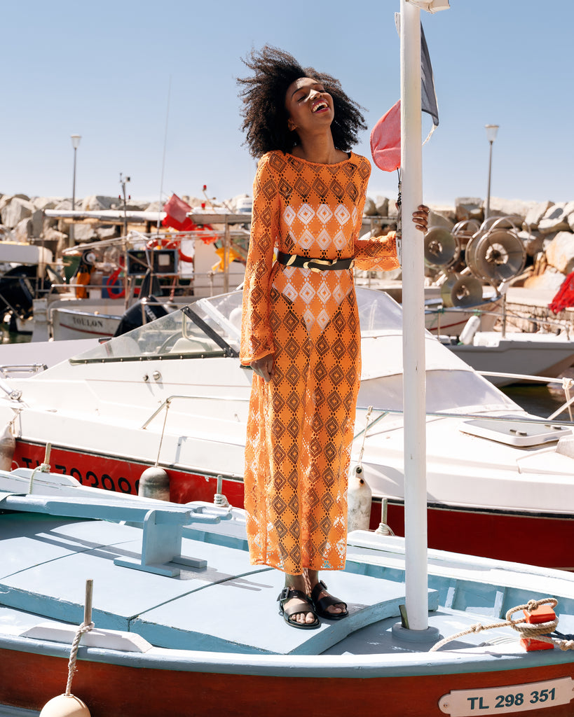 Femme en tenue estivale, une robe en crochet orange et un maillot blanc avec des sandales Vanessa Wu. Elle est debout sur un bateau.