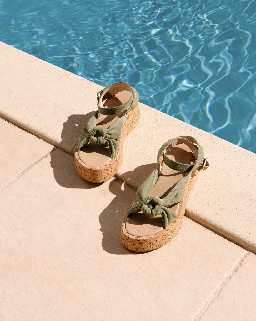 Sandales vert amande à plateforme, de la marque Vanessa Wu , posées sur le bord d'une piscine.