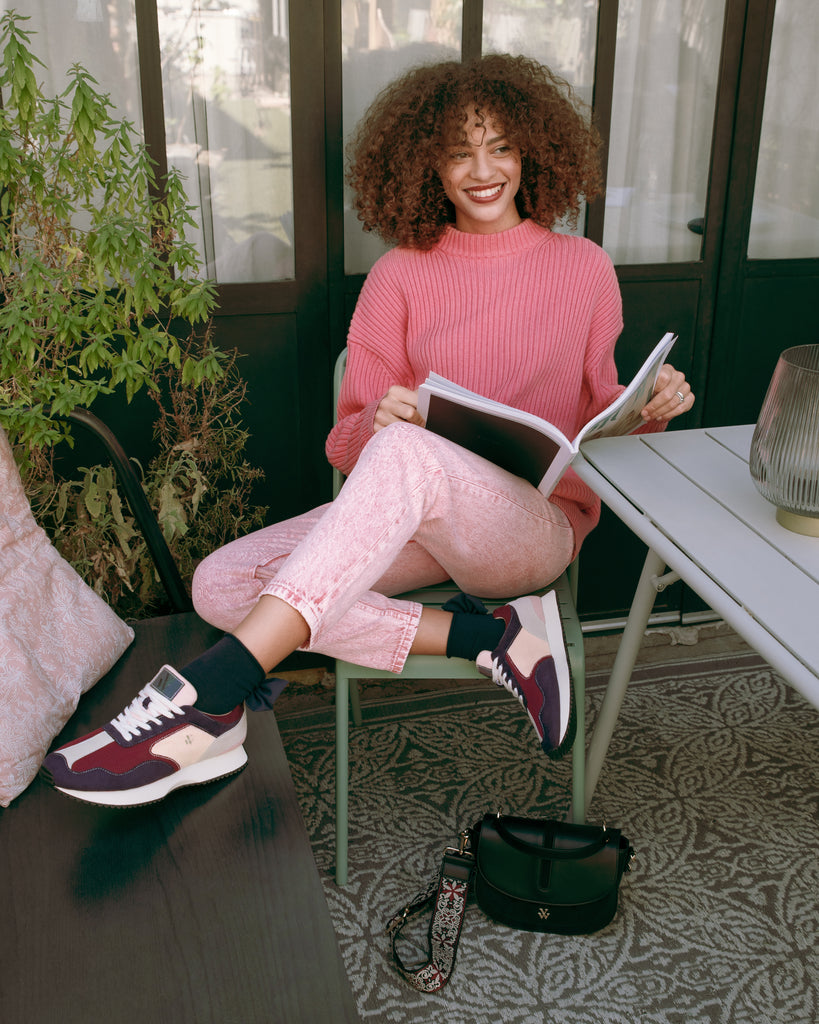 Terrasse ensoleillée avec un look monochrome rose bonbon, des baskets en suédine rose pâle et un sac bandoulière