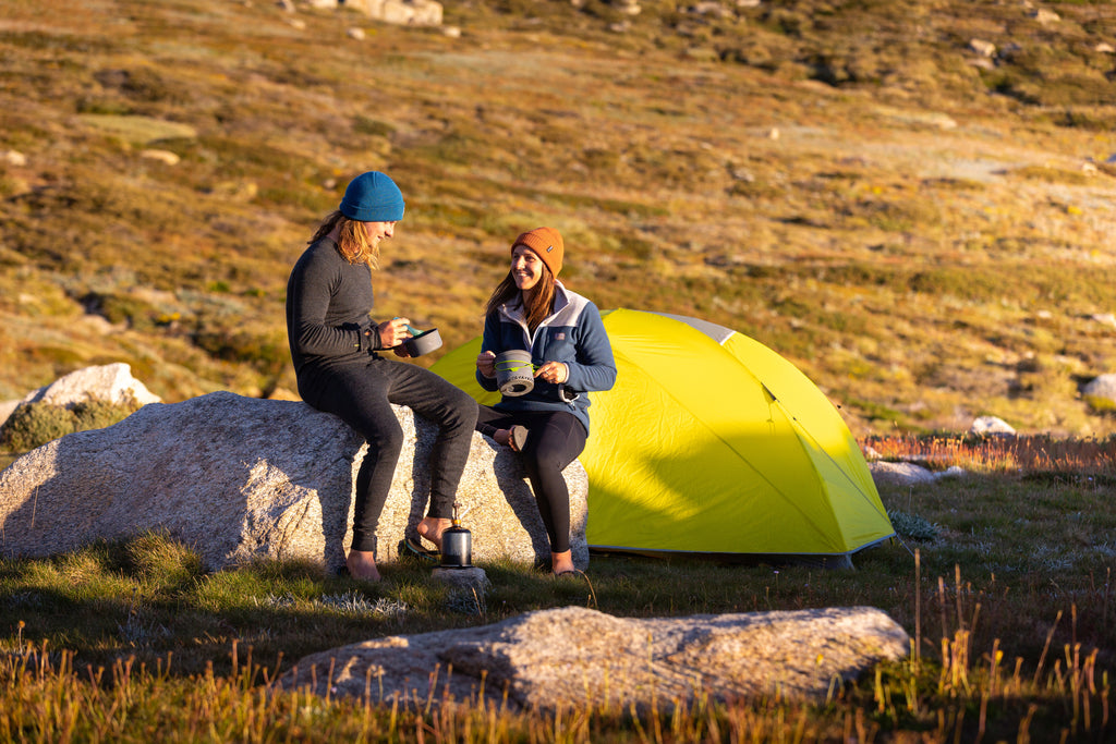 Man and women sitting on rock outside tent wearing Merino thermals and fleece midlayer