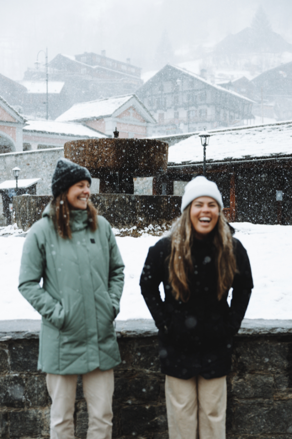 Two girls stand in the snow at Alagna Valsesia, smiling and laughing