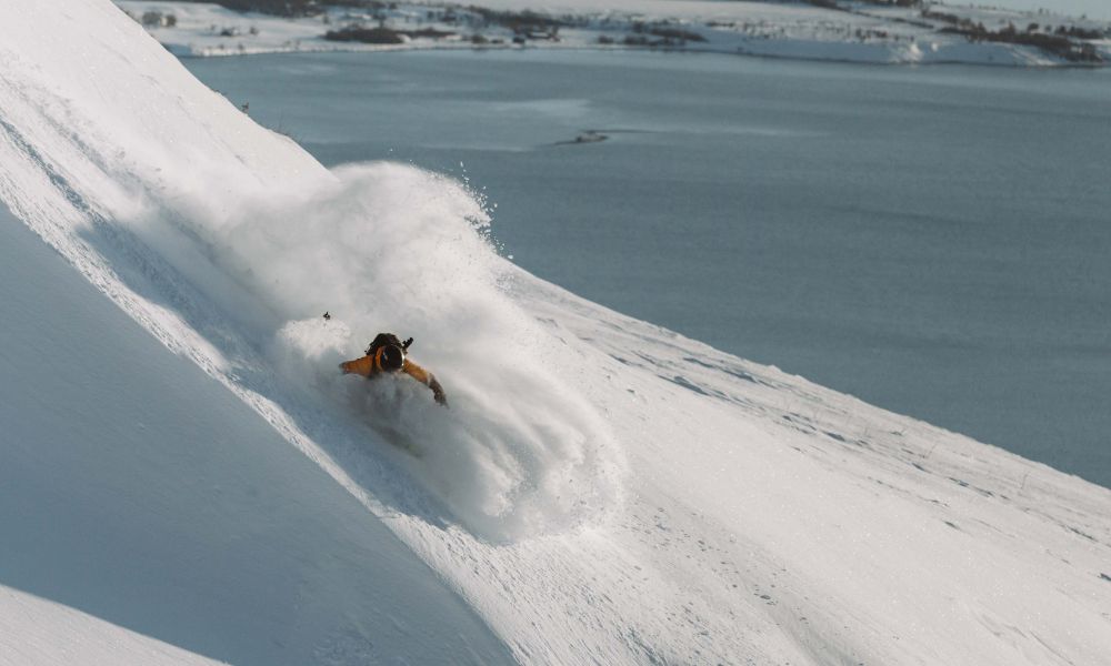 Skier making pow turn along a cornice with fjords in background