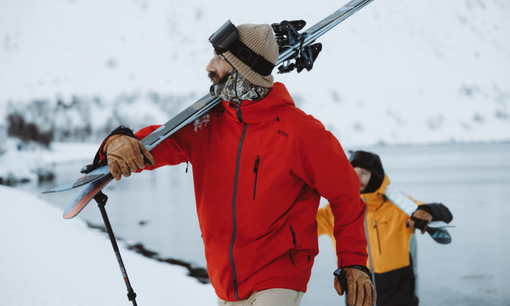 Man in red snow jacket walking with skis on shoulder