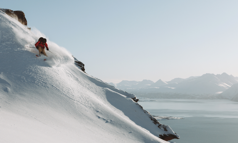 Skier on edge of cliff making a turn with fjords in background