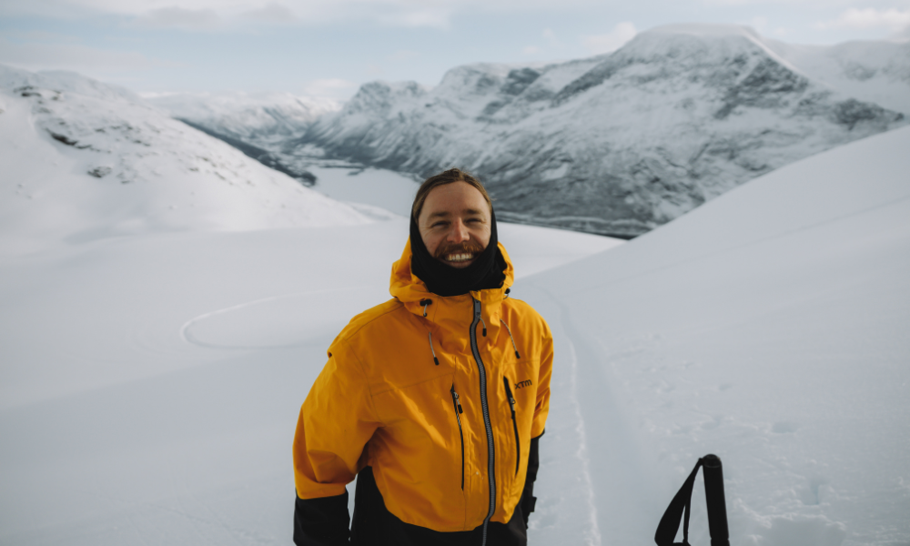 Man in yellow ski jacket surrounding by mountains smiling at camera 