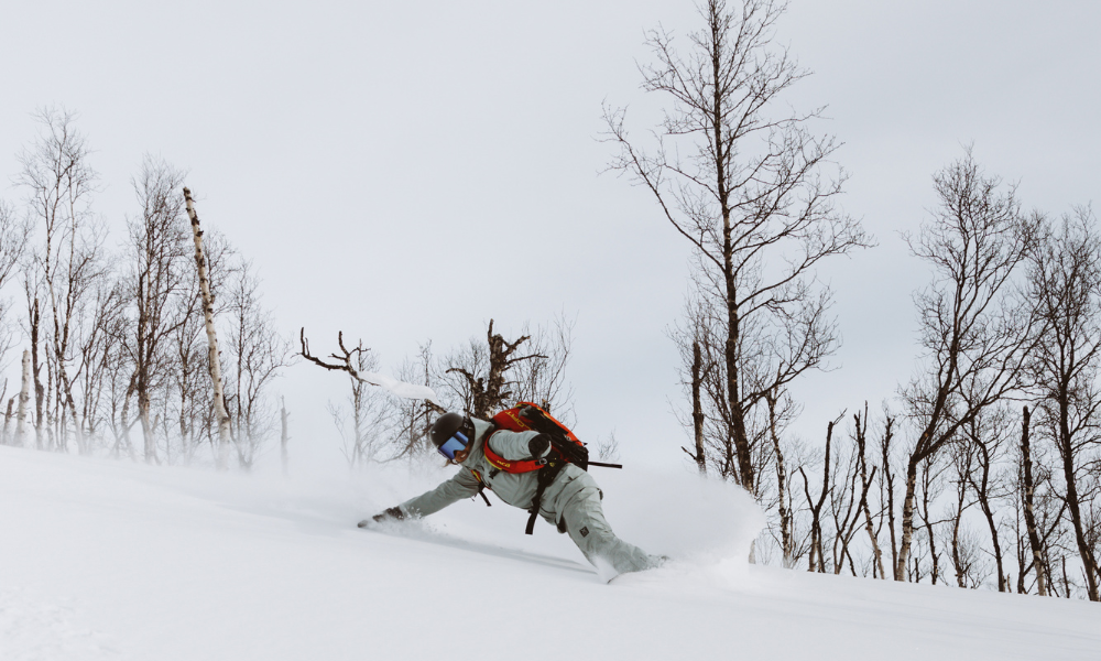 Snowboarder in green outerwear making a pow turn