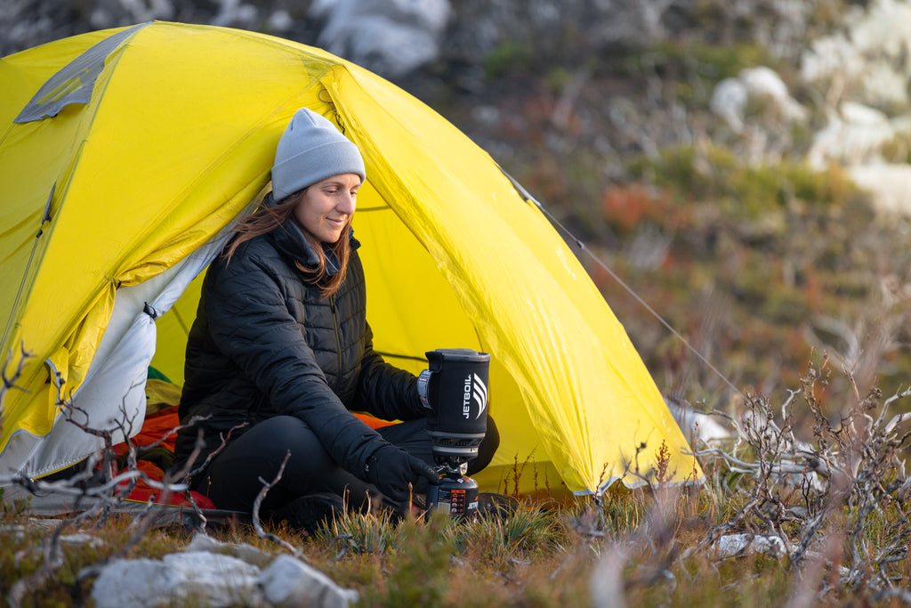 Women using portable cooker outside tent.