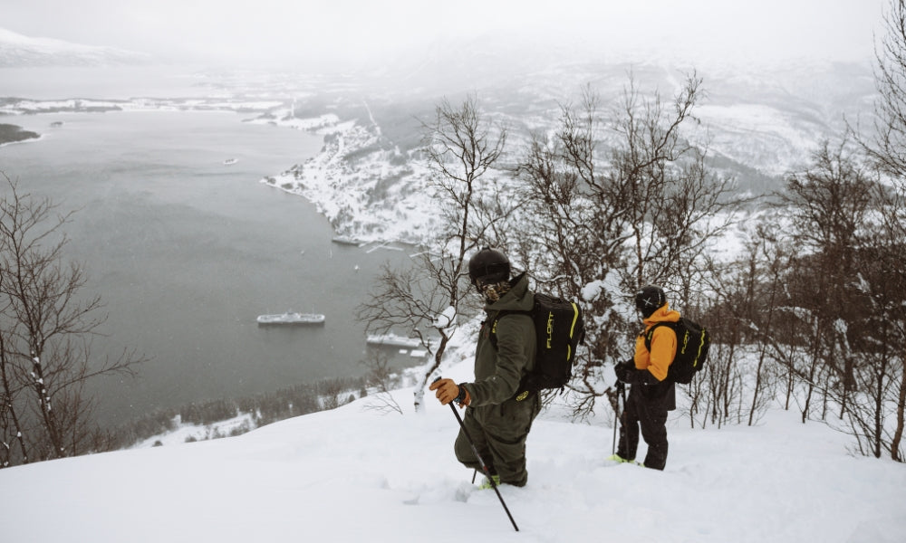 Two skiers on edge of cliff looking down to Norwegian fjords