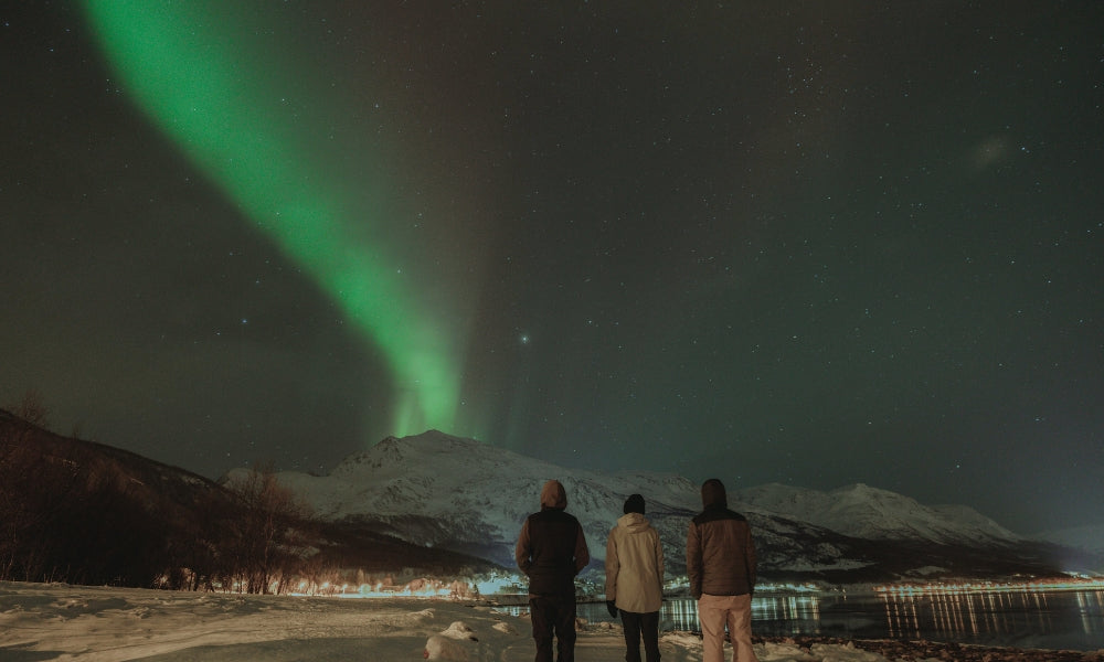 Three people at night watching Aurora Borealis behind a mountain