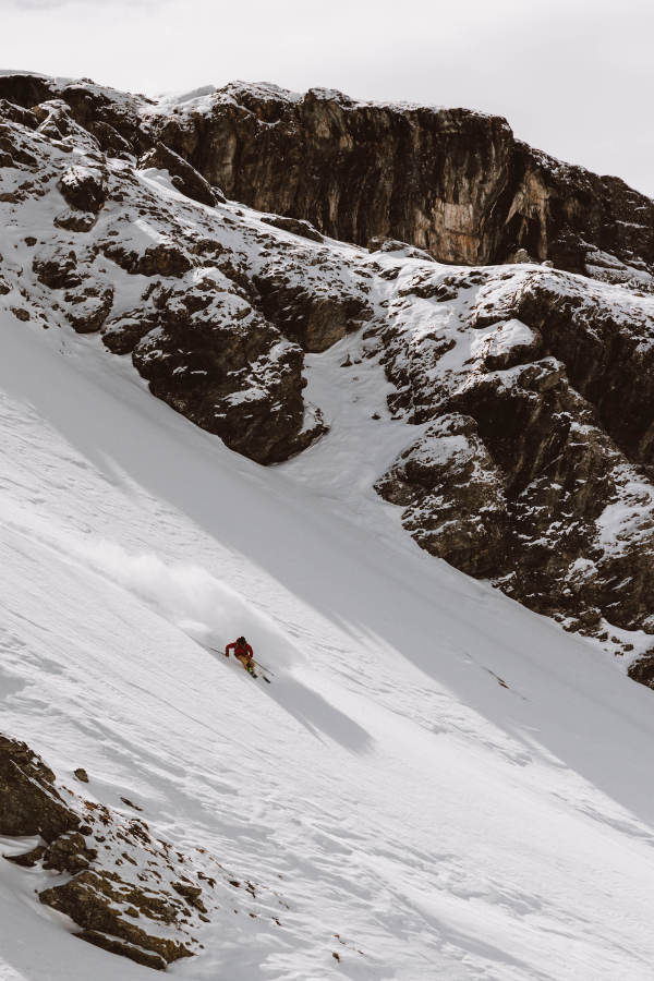 Skier in pow turn with mountain rocks behind