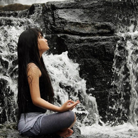 Asian woman meditating near a waterfall
