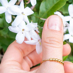 Gold adjustable fidget ring with beads on a woman's hand next to a white flower