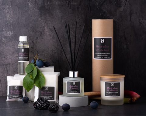 Henry and co home fragrance black plum and rhubarb fragrance collection, reed diffuser, scented candle, reed diffuser refill and wax melts surrounded by fresh fruit