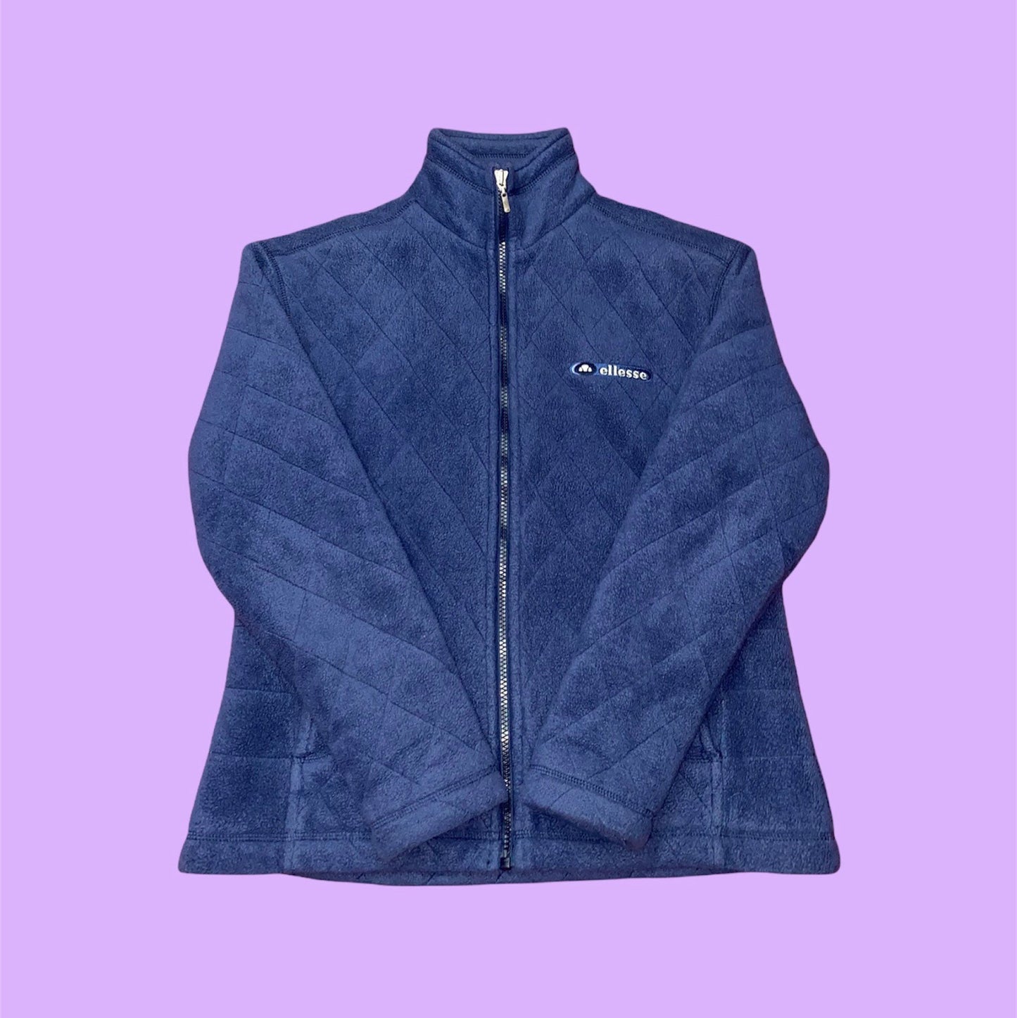 navy zip ellesse jacket with embroidered text logo on chest shown on a lilac background