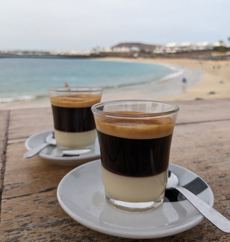 two cafe bombon coffees with a beach in the background