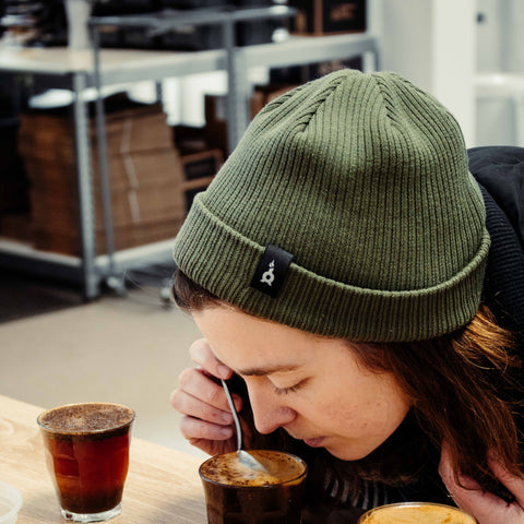 Woman wearing chimney fire coffee bean green beanie tasting coffee