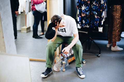 Man dressed in POP Trading Company clothing sitting on skateboards