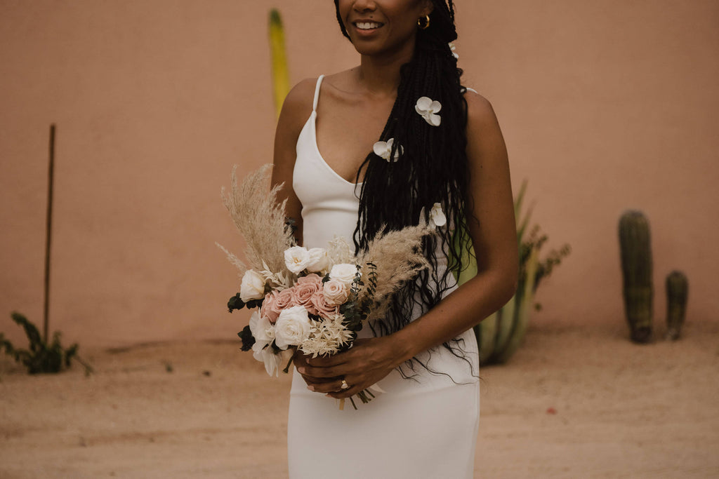 A bride holds a bouquet with white and blush roses that complement the flowers in her hair.