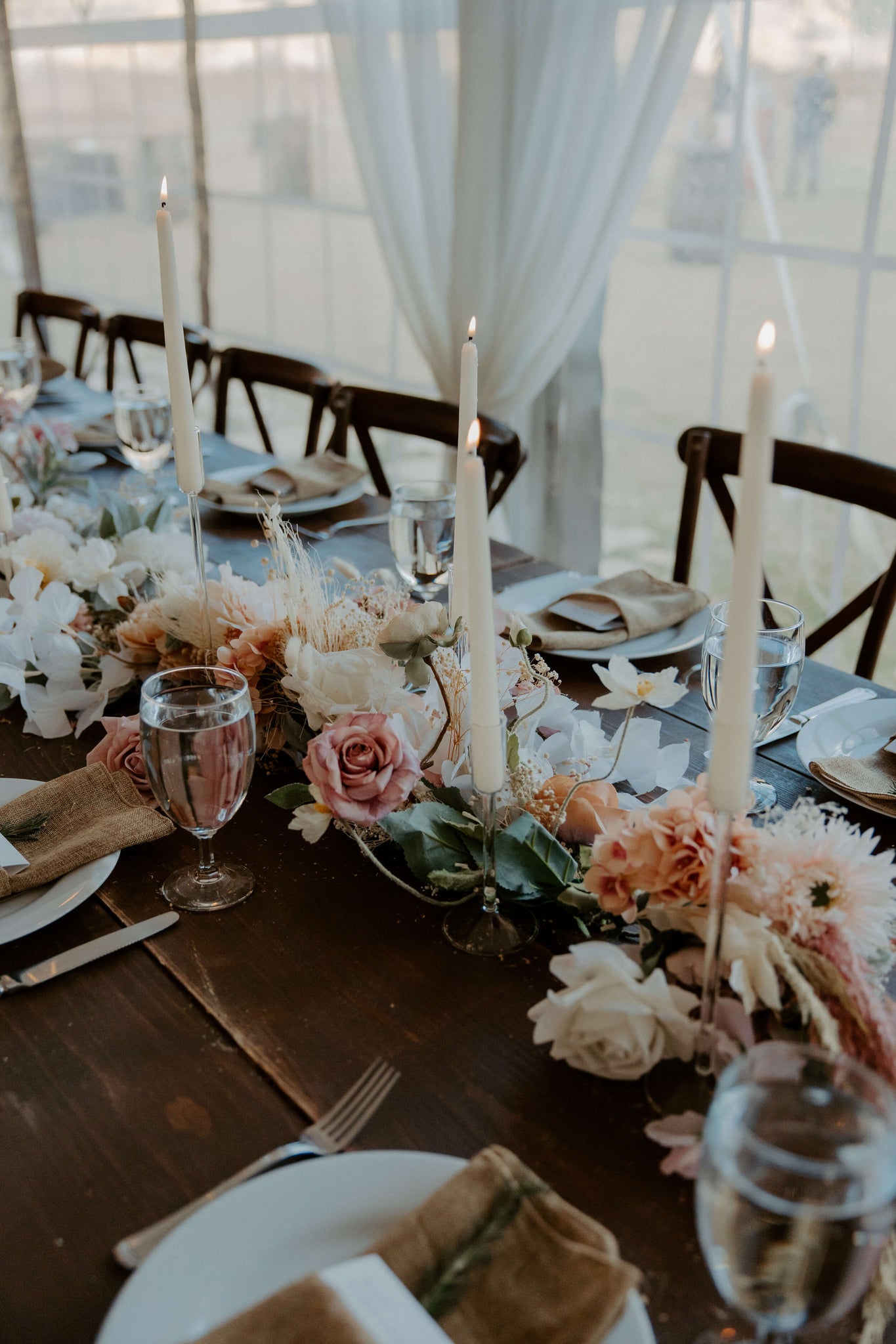 An intimate table setting by Hidden Botanics, with lit candles, a floral runner in pastel tones, and elegant tableware.