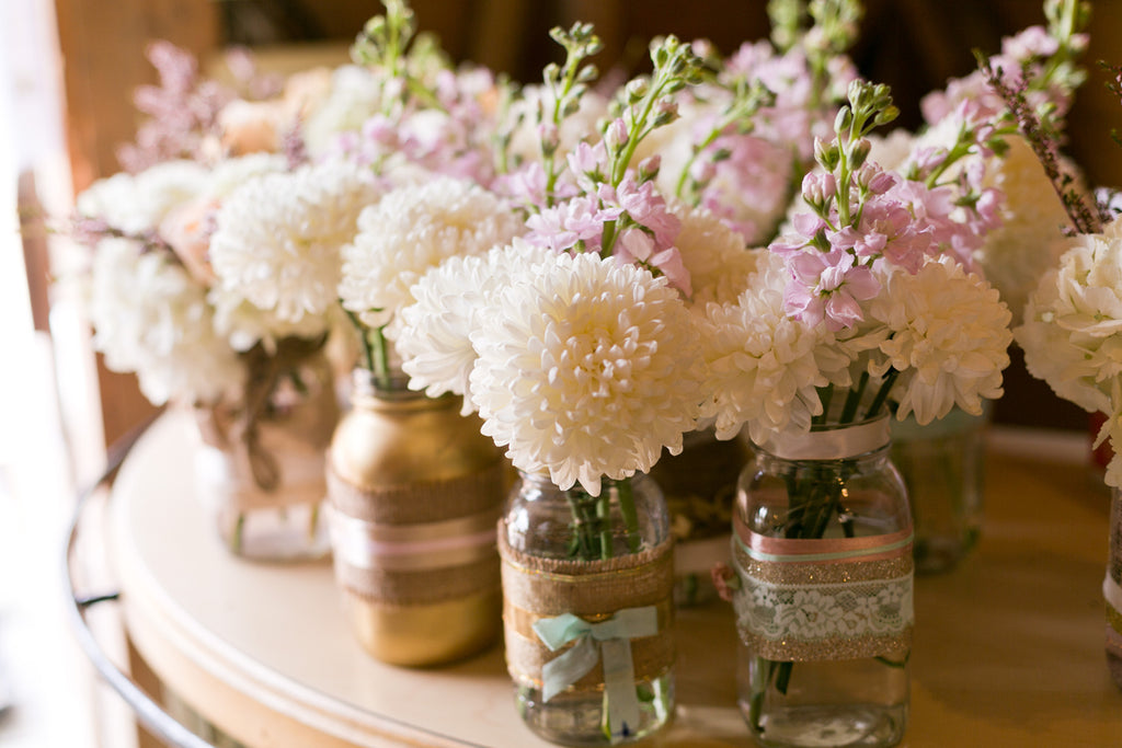 A collection of glass jars full of white dahlias and pink stocks.