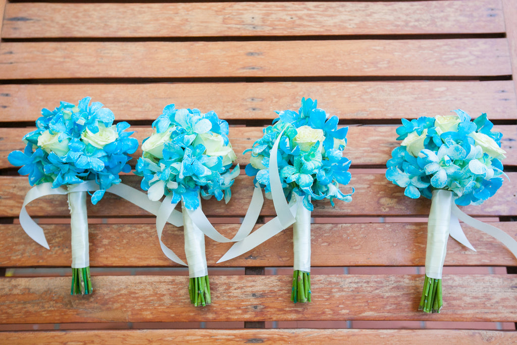 Several small bunches of blue sweet peas and white rose bouquets are placed on a wooden backdrop.