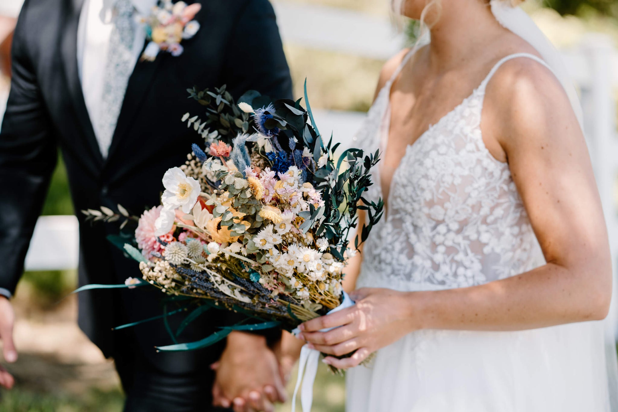 Bride and groom walk hand in hand with Hidden Botanics dried wildflower bridal bouquet.