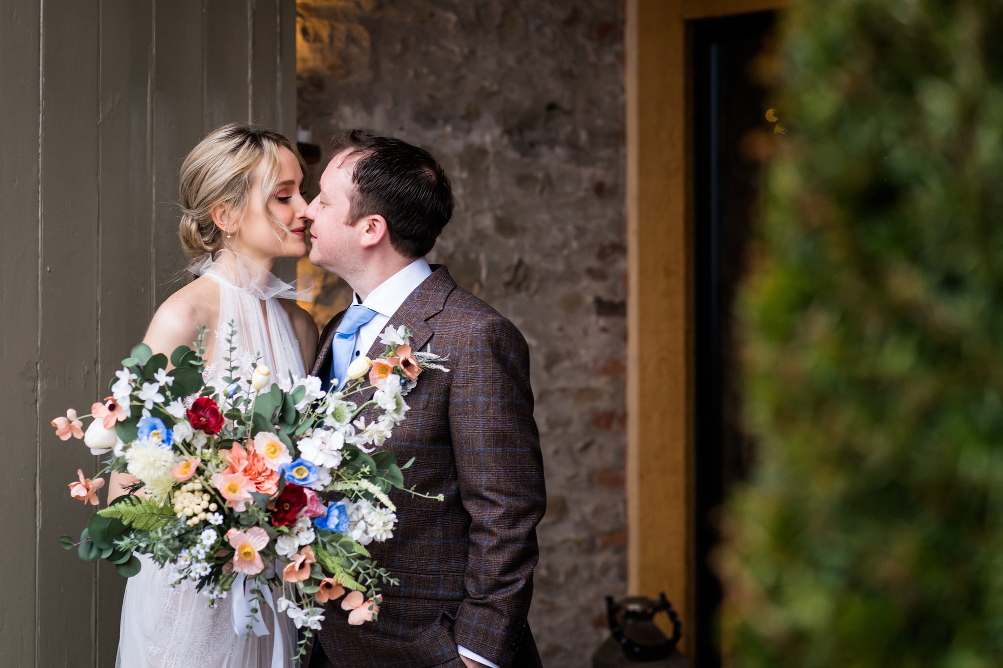 Newlyweds kissing with the bride holding a vivid bouquet by Hidden Botanics.