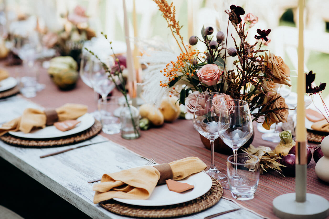 A rustic wedding table setting complemented by a centerpiece of dried flowers in warm hues, including roses and pampas grass, creating a romantic and bohemian atmosphere.