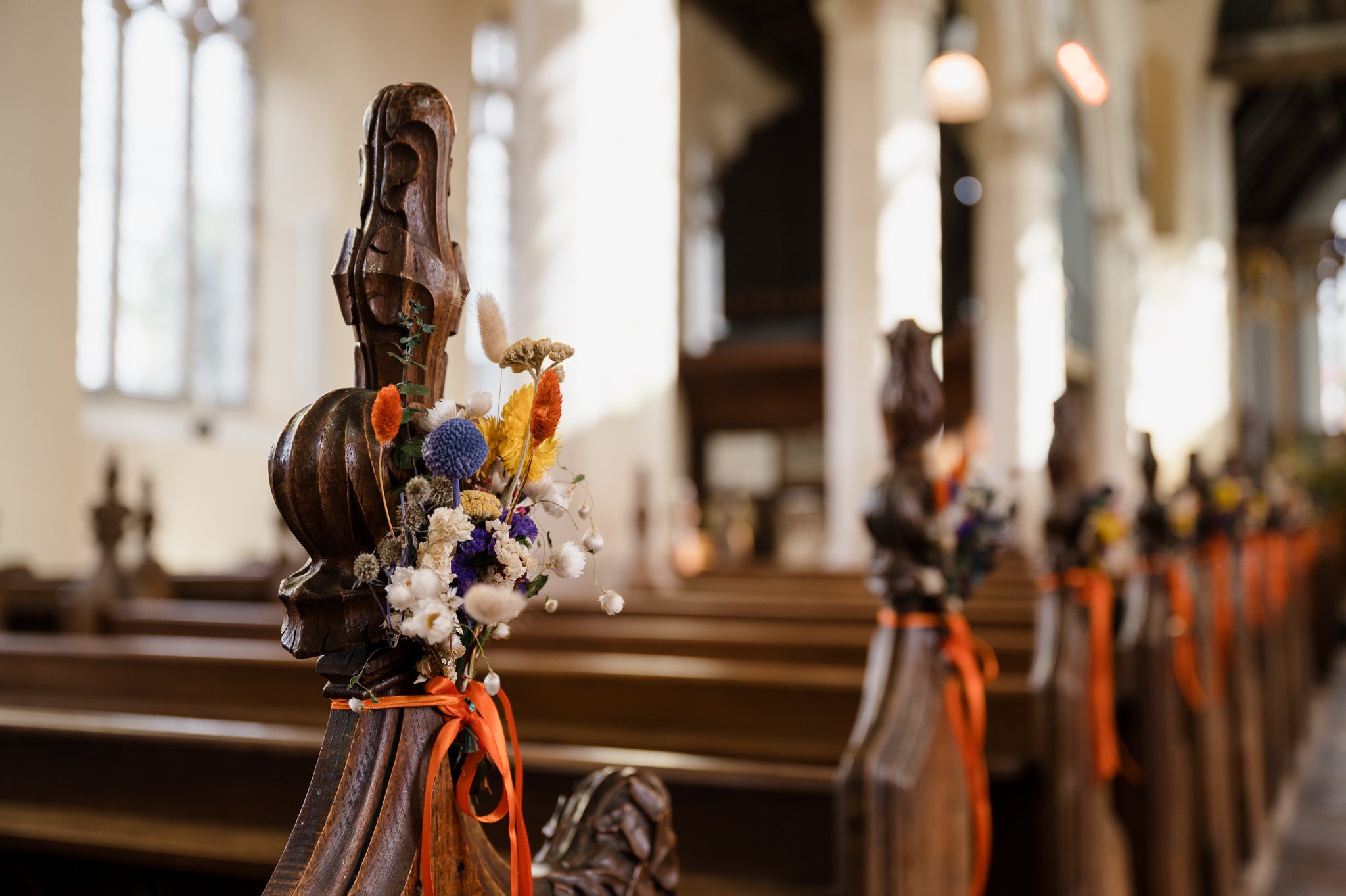 Colorful Hidden Botanics floral arrangements brighten the wooden pews of a church, adding a festive touch to the atmosphere.