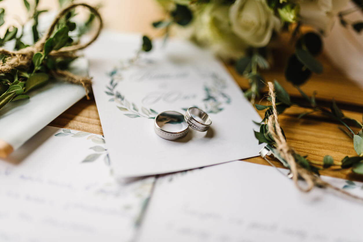A picture featuring a pair of silver wedding rings resting on a card, alongside floral decorations and bundled herbs, evoking a romantic and sophisticated ambiance.