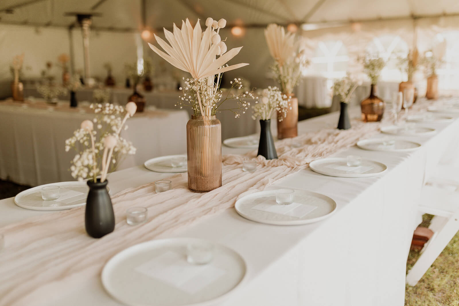 A monochromatic table setting with wooden vases and pale florals under a tented venue, creating an elegant atmosphere.