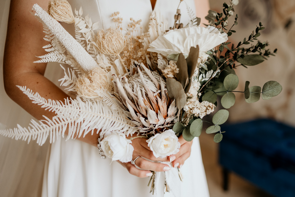 A bride’s hands are seen holding a large dried flower wedding arrangement from Hidden Botanics.
