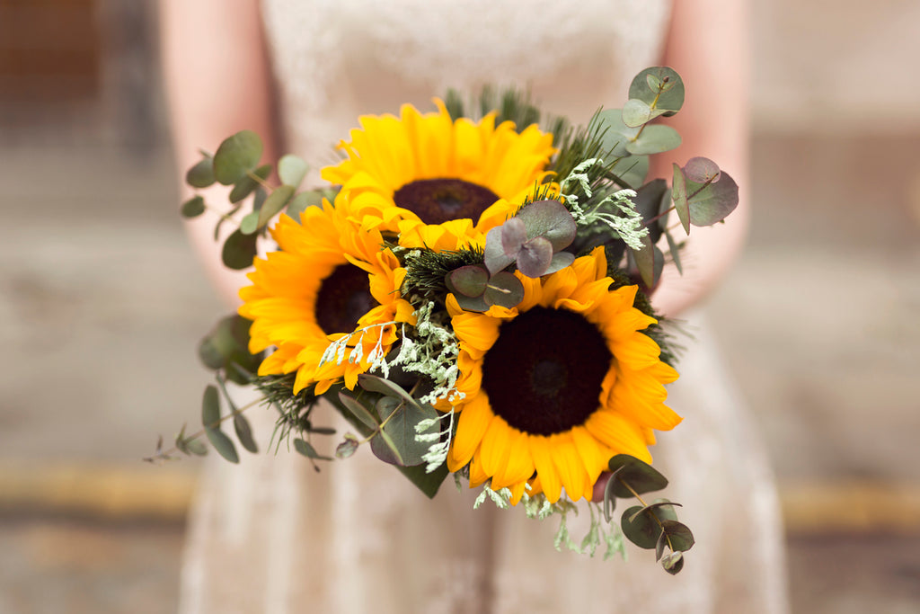 A bride holding a bouquet of sunflowers and eucalyptus.