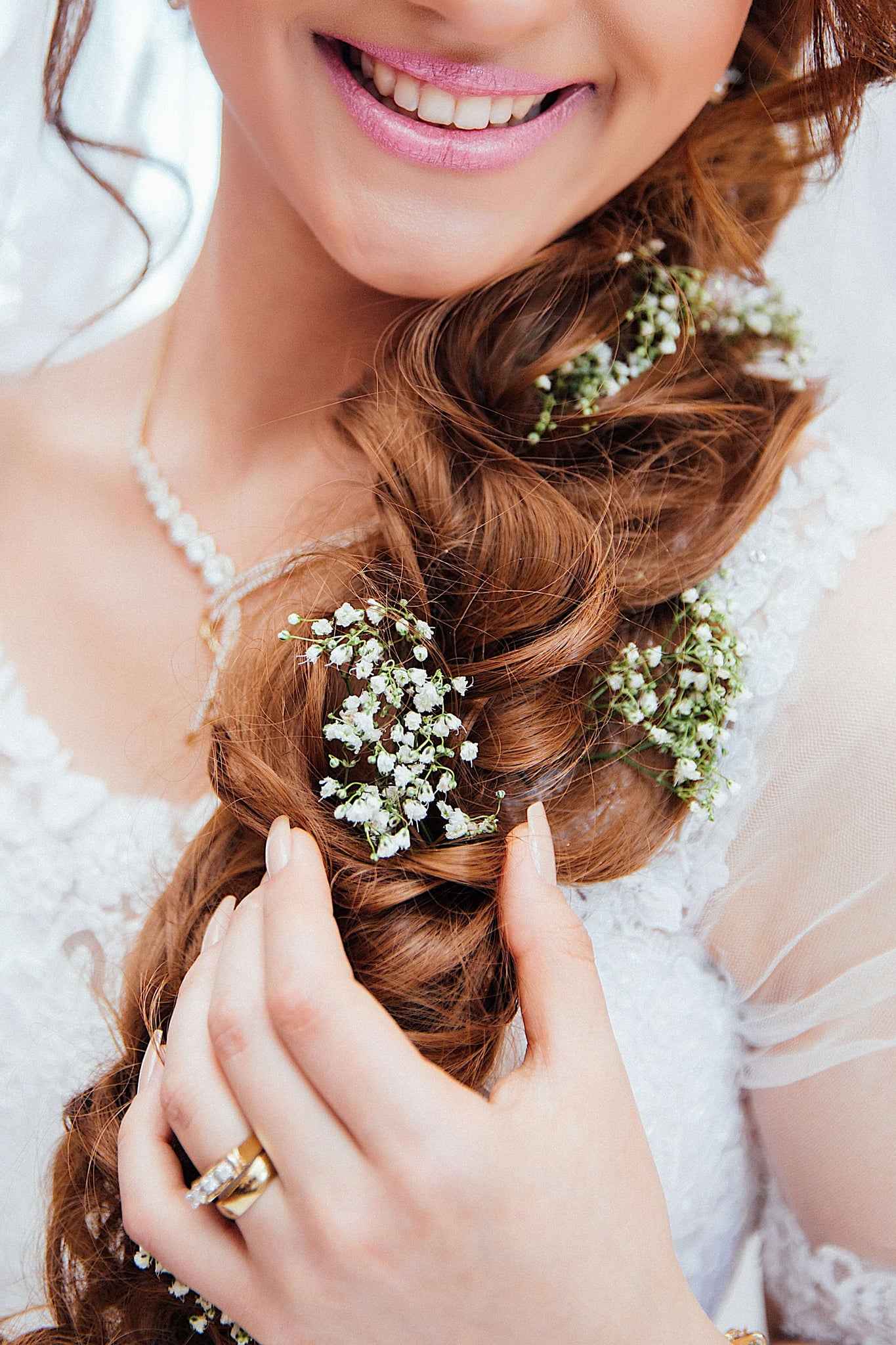 A close-up of a bride's hairstyle, showcasing a cascading side braid interwoven with clusters of tiny white flowers.