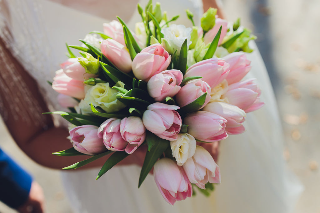 A bride holding a large bouquet of pink tulips.